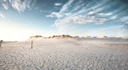 Evening view on small sand dune with green grass. Sandy beach at sea coast. Blue sky with white clouds. Sunset time.
