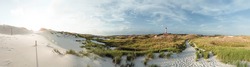 Wide panoramic evening view on sand dunes in North Sea coastal landscape. Striped naval lighthouse in distance. Summer vacation, holiday at sea concept.