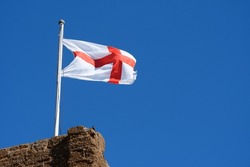 St George England flag fly's against a blue sky from the top of a historical building. Billowing  in the strong breeze. Copy space.