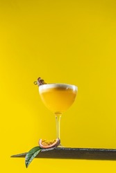 Glass of fresh passion fruit Martini cocktail on bright yellow background. Spring summer art drink food concept.