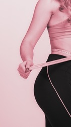 Young beautiful girl measuring her slim fit body, monochrome image with pink tint