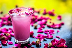 Popular Indian & Asian Summer drink on wooden surface i.e. Gulab falooda or gulab ka sherbat with some rose petals on black colored shiny surface.