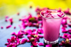 Popular Indian & Asian Summer drink on wooden surface i.e. Gulab falooda or gulab ka sherbat with some rose petals on black colored shiny surface.
