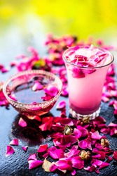 Rose falooda or rose shake in a transparent glass along with some rose syrup in another bowl on wooden surface,Popular summer and ramazan or ramadan drink.;