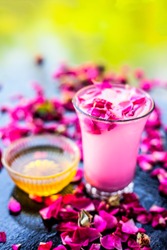 Rose falooda or rose shake in a transparent glass along with some honey in another bowl on wooden surface,Popular summer and ramazan or Ramadan drink.