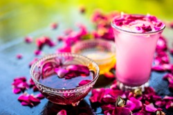 Rose falooda or rose shake in a transparent glass on wooden surface along with some honey and rose syrups in different bowls.Some rose petals on the glass also for as garnish.