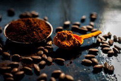 Coffee face mask for treating oily skin and for skin whitening on a black colored shiny surface consisting of some coffee beans powder, turmeric powder, and yogurt.