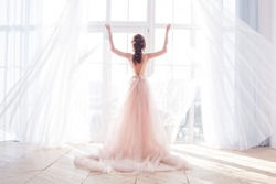 Young attractive woman standing by the window. Bride`s morning boudoir