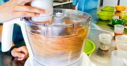 Electric food processor in fast spinning action while mixing a variety of ingredients together. The process renders the mixing bowl sample contents blurry.