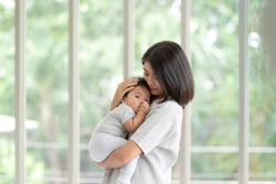 Portrait beautiful young Asian mother holding and hugging her newborn baby in living room. Healthcare and Happiness love asia woman lifestyle mother's day concept with copy space.
