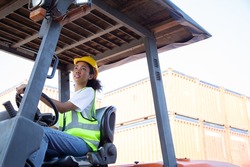 Close up happy female worker driving forklift African-American woman with safety uniform and yellow hard hat  driving forklift and work at warehouse container shipping construction site import export.