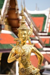 A golden Kinnara Statue half-human and half-Bird at the Wat Phra Kaew temple in Bangkok, Thailand (Focus on Foreground Blurry Background)