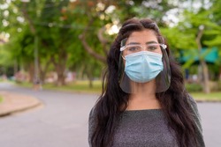 Face of young Indian woman wearing mask and face shield at the park outdoors