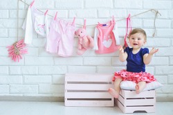 Portrait of a cute little smiling girl with baby clothes hanging on background