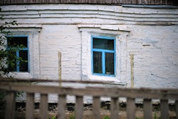 Facade of an old rural house with blue window frames. Ancient architecture in greek national colors. Old deformation of the wall structure caused by subsidence.