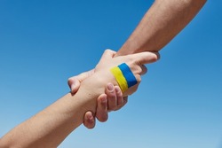 Lend a hand help painted in ukrainian flag colors against blue sky. Stand with Ukraine