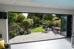 Beautiful garden and patio in summer seen from stylish designer room through bifold doors.
