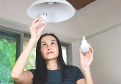 Asian woman  changing light bulb , from spiral  light bulb to LED light bulb. Slective focus on woman eyes.