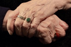 The hands of an elderly woman. Wrinkles are the lines of life. Well-groomed aristocratic outlines. Arms crossed on a dark background.