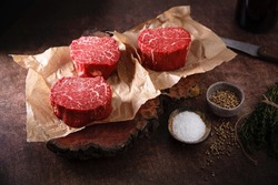 Rounds of raw meat sit on butches paper next to small bowls holding salt and other spices