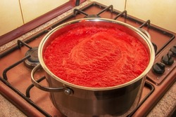 A woman prepares fresh healthy juice from tomatoes. Freshly made tomato juice is boiled in a saucepan and preserved for long-term storage. Diet concept for a healthy lifestyle.