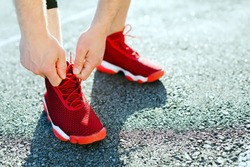 Sport concept, red sneakers for running. Man tightening lacings on his sneakers, no face. Legs in professional sport shoes, closeup. Outdoors, sunlight, stadium