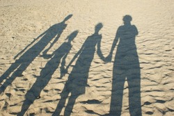 Shadow on the sand from the family , parents and children holding hands. Happy young family. The concept of light and shadow, happiness, vacation, travel, family values, love.