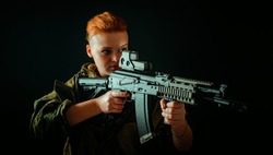 Portrait of young woman with red hair, young girl takes aim at the sight in military uniform