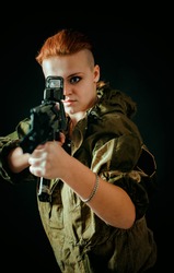 Young woman with red hair, hold machinegun in hands in military uniform. Vertical photo