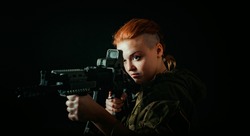 Woman with red hair, hold machinegun and takes aim at the sight in military uniform. horizontal background
