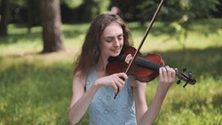 A young girl plays the violin in the city park.
