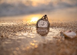 An old pocket watch dropped on the sand, in warm light and bokeh background - thinking and controlling the concept of time.
