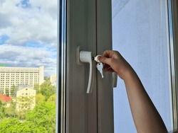Small child opens window security lock with key. Child is in danger and the safety and protection of children.