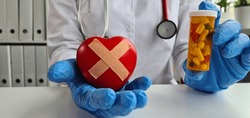 Cardiologist holds red broken wounded sick heart and pills. Treatment of cardiovascular diseases