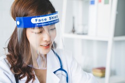Medical healthcare beautiful Asian doctor wearing face shield mask protection from infectious disease virus bacteria germs coronavirus covid-19, safety protection working in hospital modern office 