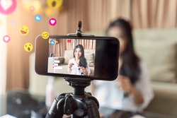 Asian businesswoman working from home live video interaction with customers using camera device vlogging selling make up products, viral internet social media influencer interacting to live audience