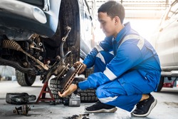 Mechanic Asian man fixing repairing car rotor spindle hub wheel automobile vehicle parts examining using tools equipment working hard in workshop garage support and service in overall work uniform
