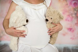 Mom hands holding two bear. Pregnant woman's belly. Twins