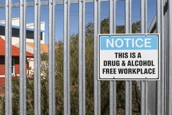 a metal black, white and blue Notice, This is a Drug and Alcohol Free Workplace warning sign on the fence of an industrial workplace