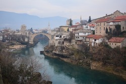 Mostar old stone bridge in historical city center and Neretva river in a foggy winter day.