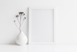 White desk with photo frame and  minimal round vase with a decorative twig against white wall. 