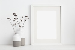 Mock up white frame and dry twigs in vase on book shelf or desk. White colors.