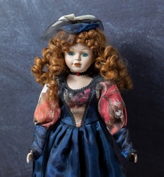 Amazing realistic vintage toy with blue eyes.The doll dressed in a red-blue dress and has a red hair. Selective focus. Porcelain doll.