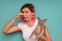 Young beautiful woman standing against blue background, holding her nose because of a bad smell coming out from the cat.