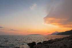 Croatian sunset with orange and red sky and a cost line with mountains and blue water.