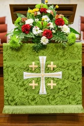 Church pulpit with flowers and green tapestry with cross symbol