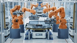 Row of Robot Arms inside Bright Plant Assemble Batteries for Automotive Industry. EV Battery Pack Automated Production Line Equipped with Orange Advanced Robotic Arms. Electric Car Smart Factory