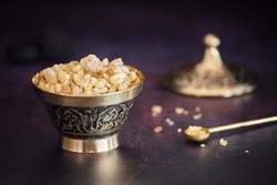 Fragrant frankincense resin (olibanum) in an incense burner  on a dark surface with brass spoon