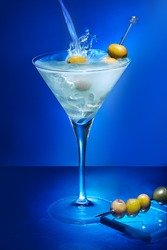 Alcoholic cocktail with olives on blue background