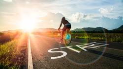 Concept of start straight and beginning for cooperation.Blurry Man ride on bike and word start written on the road at sunset add lens flare.Concept of challenge or career path,business strategy.